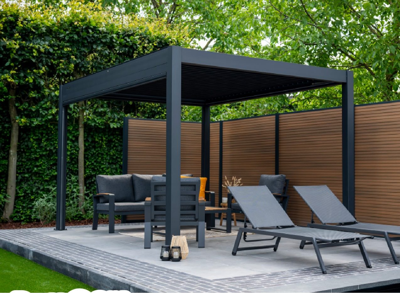Aluminium pergola met lamellendak boven een loungeset en twee ligbedden, tussen een houten schutting en een haag