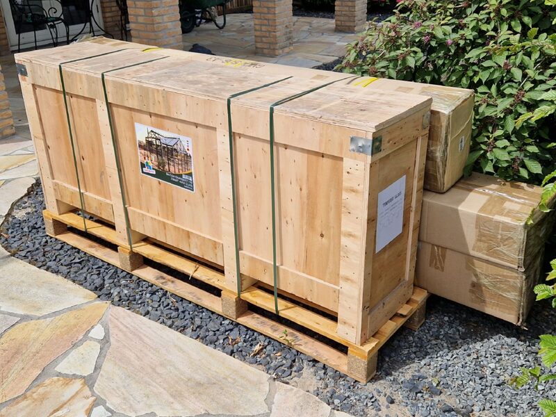 Een houten kist en twee dozen met het bouwpakket op een pallet, naast het terras
