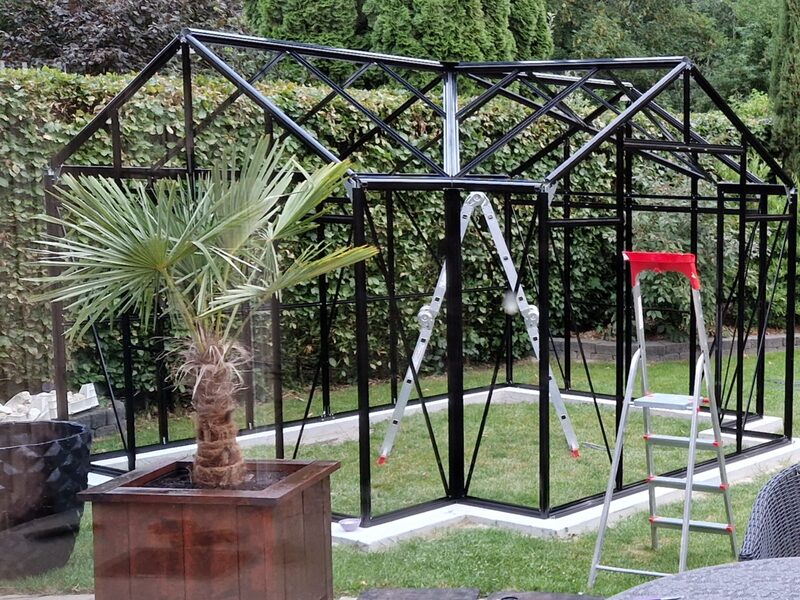 Het aluminium frame van de tuinkas staat, met twee trappen ernaast